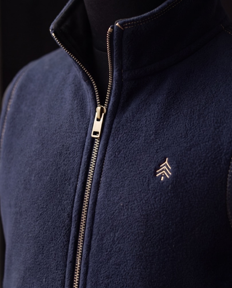 A close view of a navy Cedar Rowe fleece, its brass zip and the embroidered cedar mark in low light.